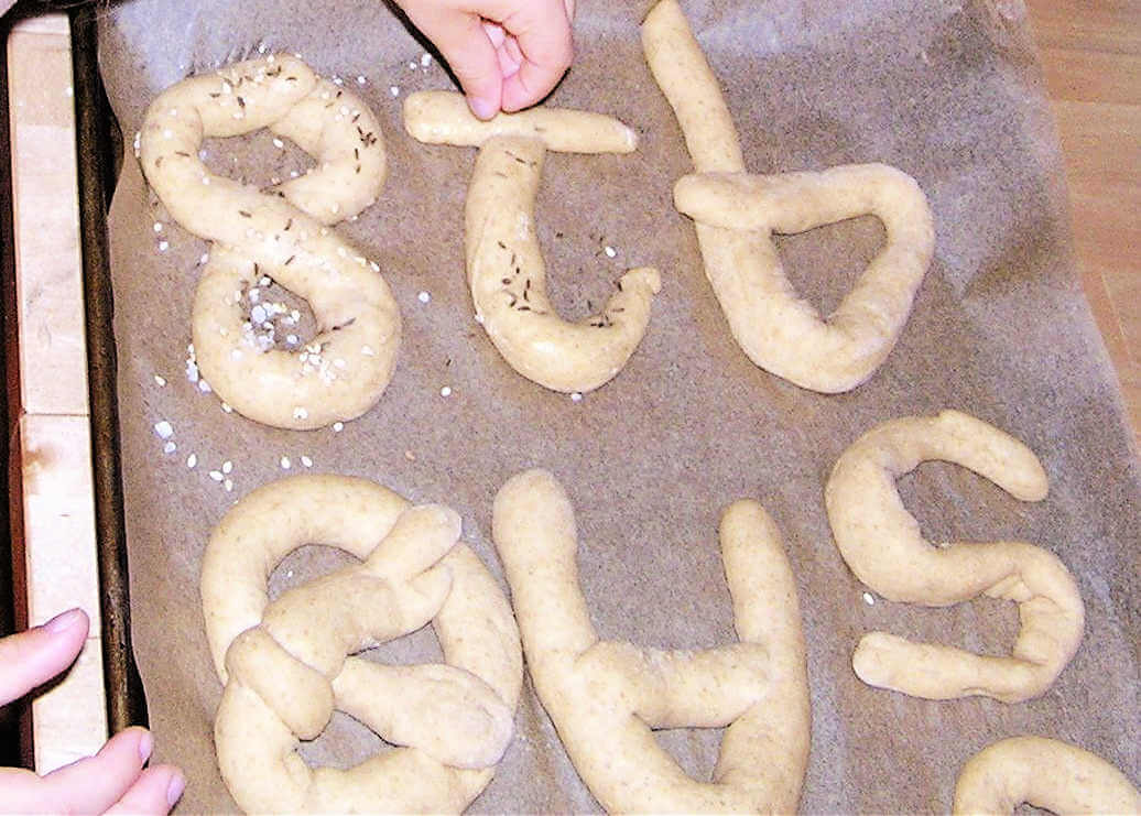 child sprinkling seeds on unbaked pretzel number and letter shapes
