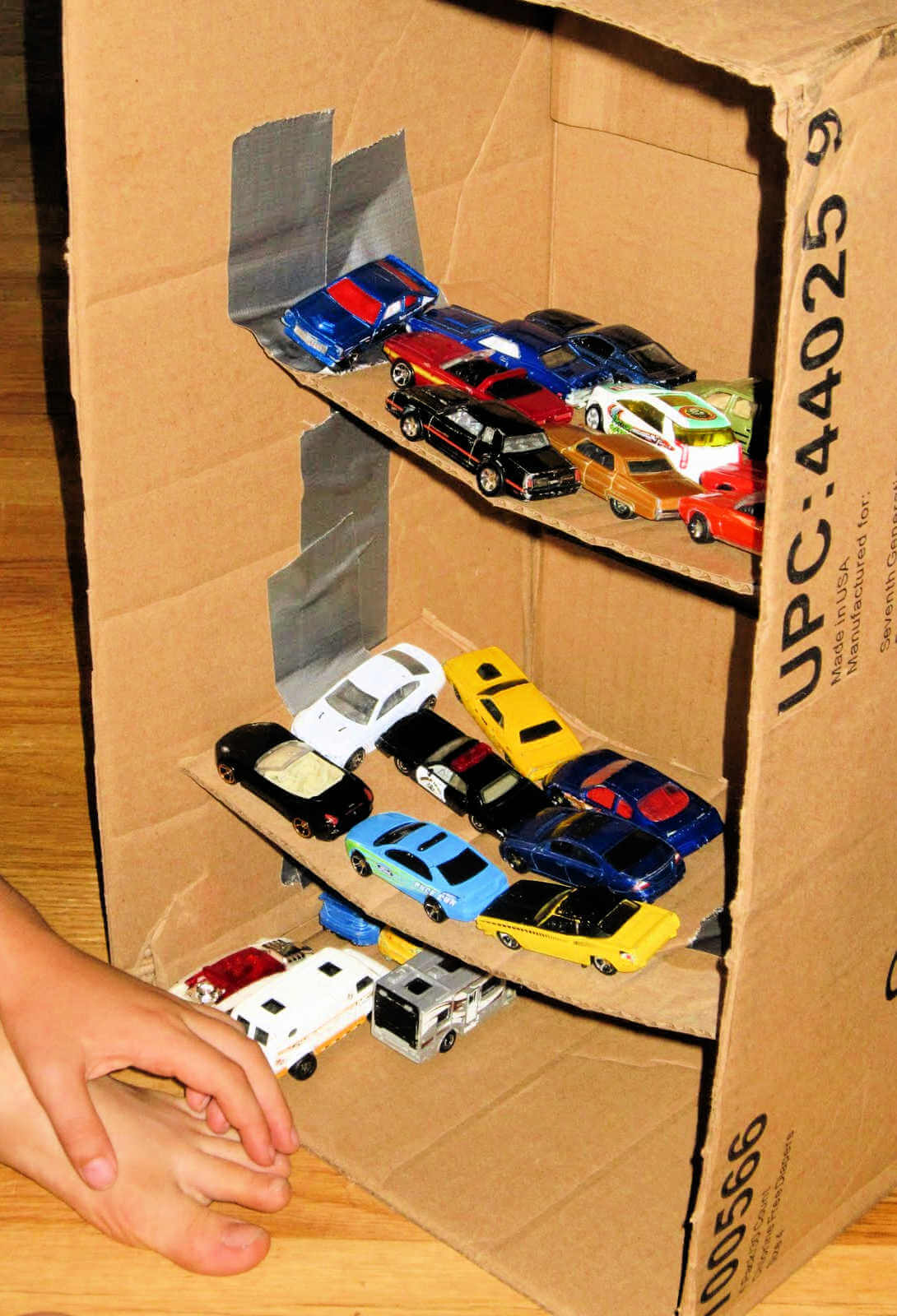toy vehicles parked inside diy parking garage made from cardboard box with three levels