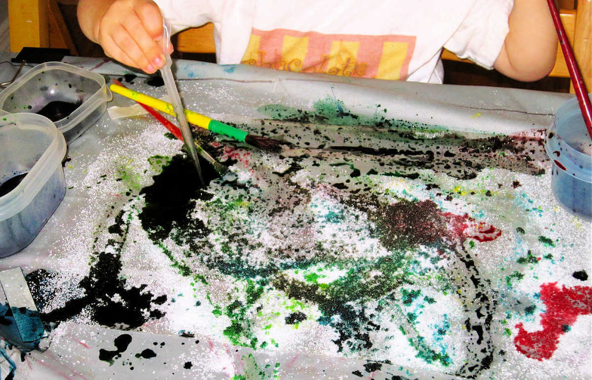 Child dropping liquid watercolors on salt covered sticky paper