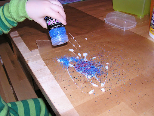 Child sprinkling glitter on wet glue.