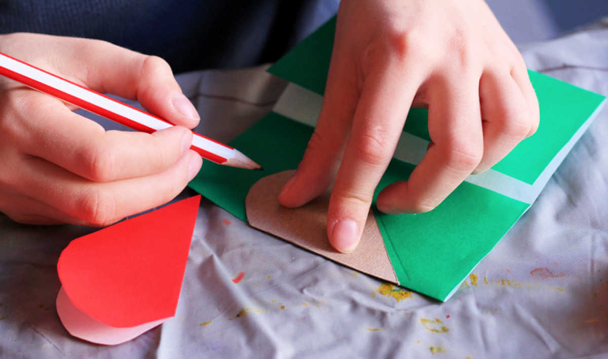 Hands drawing a half-heart on green paper using a cardboard template.