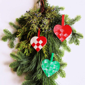 Pine branch decorated with three paper woven heart ornaments.
