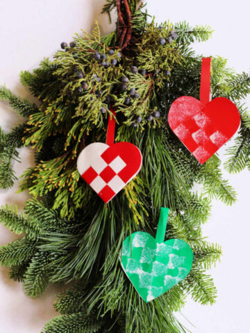 Pine branch decorated with three paper woven heart ornaments.