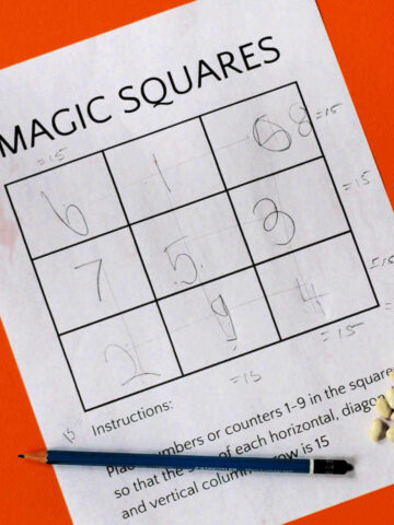 Magic square printable with large grid of nine squares filled in with pencil drawn numbers. Blue pencil and pile of beans nearby.