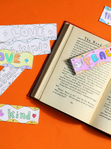 Paper bookmarks with kindness and peace messages next to and on top of open book.