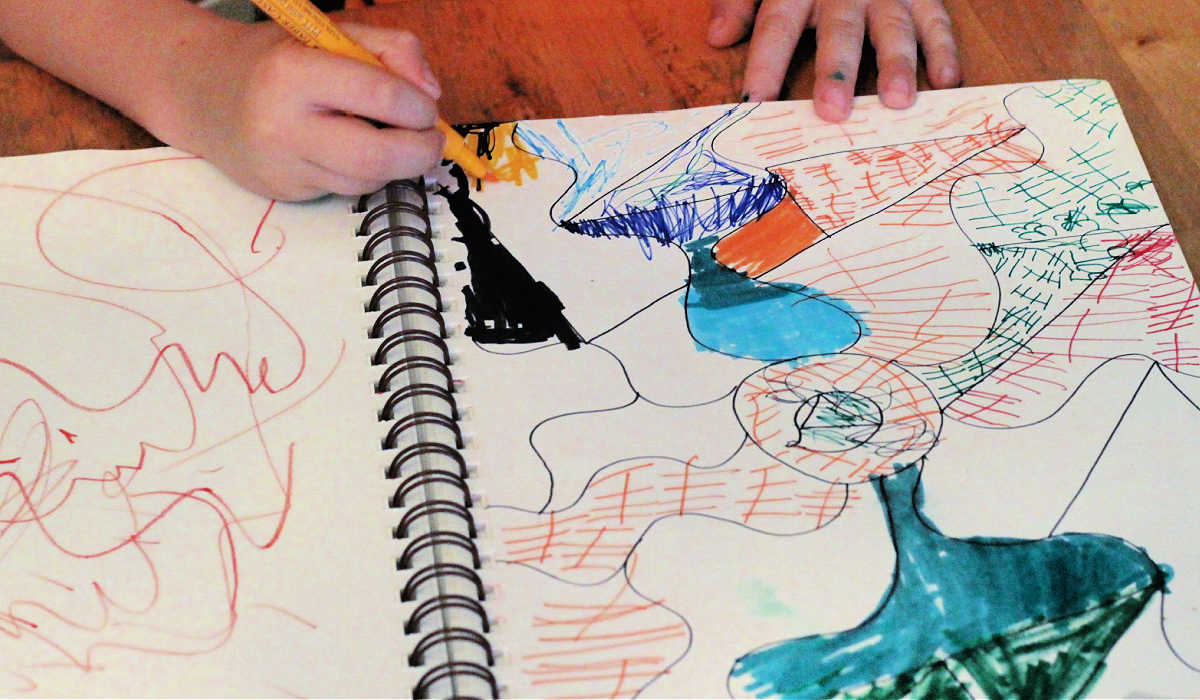 Child's hands drawing designs in art journal.