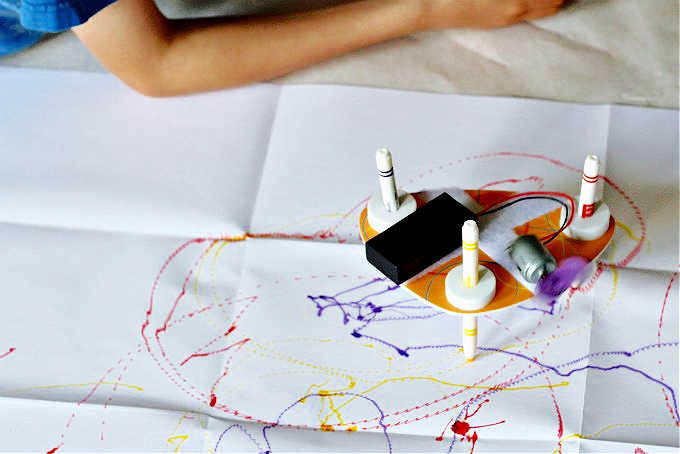 Drawing robot drawing on white paper with yellow, purple and red markers.