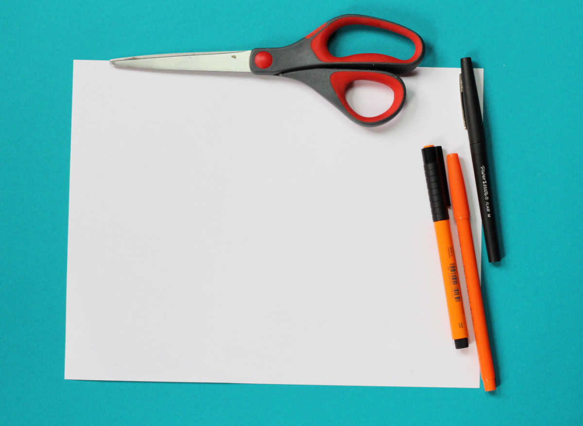 Blank piece of white paper, three pens and a pair of scissors.