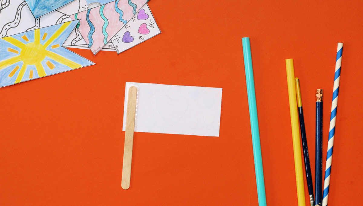 Craft stick taped to back of small rectangular flag, next to assortment of colorful paper flags and straws.