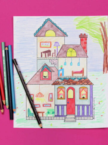 Dollhouse coloring page, colored in and sitting on pink background next to colored pencils.
